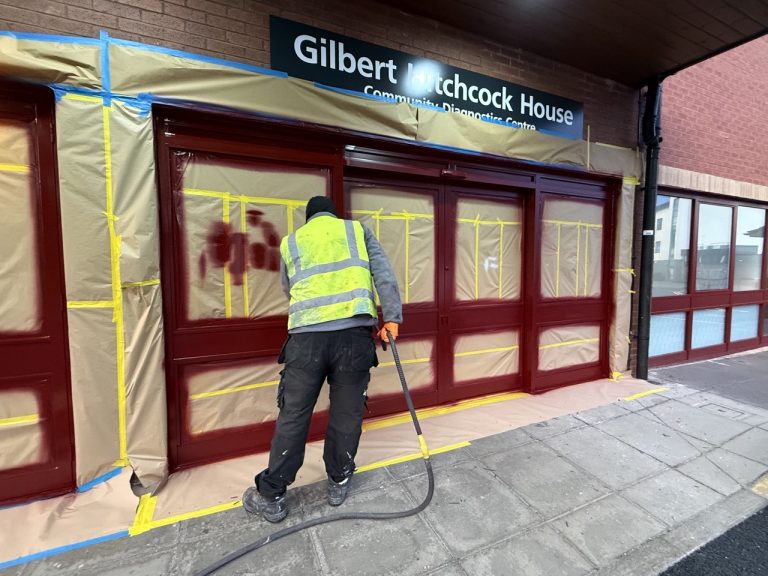 Operative spraying masked curtain wall frames at a building entrance in Bedford